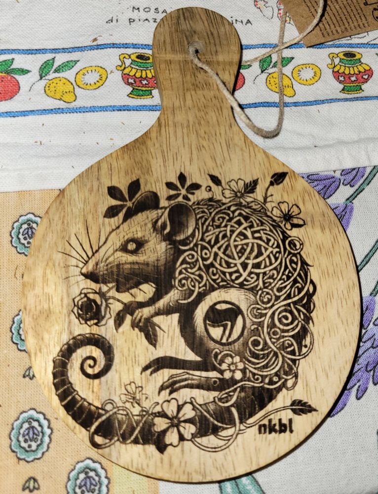 Un rat tenant une rose ,son.corps de d'élite en entrelacés tribaux,un drapeau antifa sur sa cuisse,gravé en noir au laser sur une planche de manguier. 