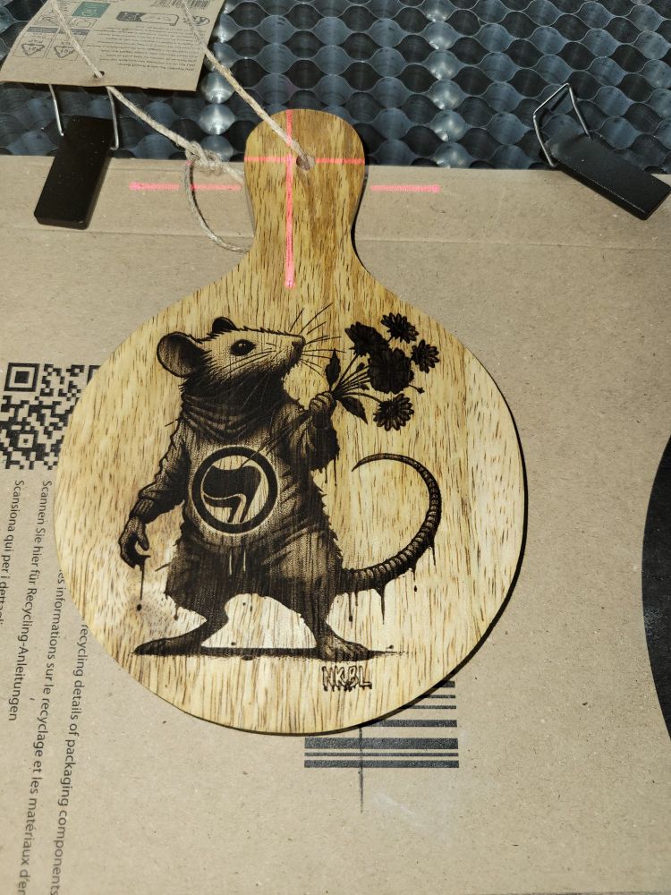 Un Rat debout avec un sweat antifa tenant des fleurs ,gravé au laser en noir sur une planche de manguier.