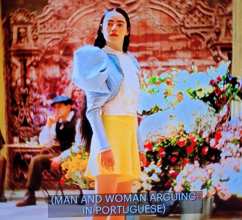 A pic of Emma Stone in Poor Things with the caption MAN AND WOMAN ARGUING IN PORTUGUESE