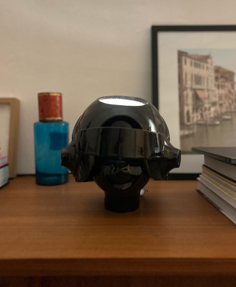 Photo d’une lampe en forme de visage portant un casque, disposée sur une commode.