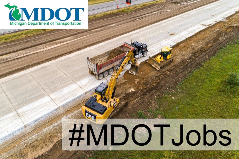 Backhoe moves sand next to new concrete on a freeway.