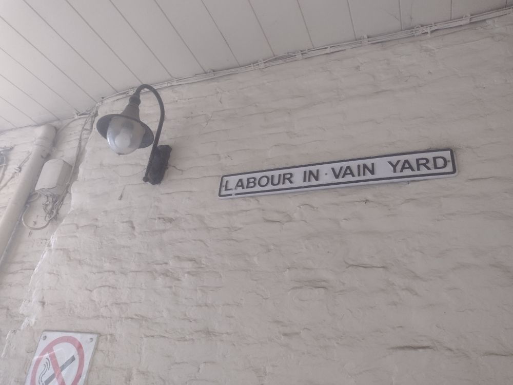 A brick wall painted grey with a street lamp and a sign saying 'labour in vain yard'