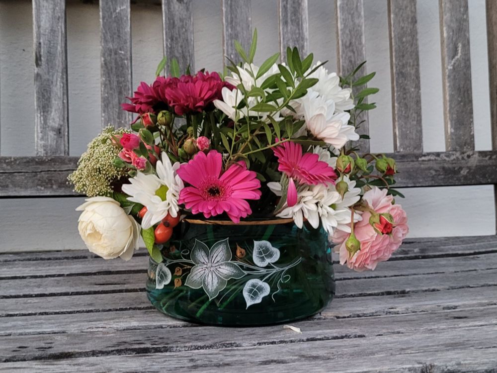 Grüne Glasschale mit weiß-rosa Blumen auf einer Holzbank.