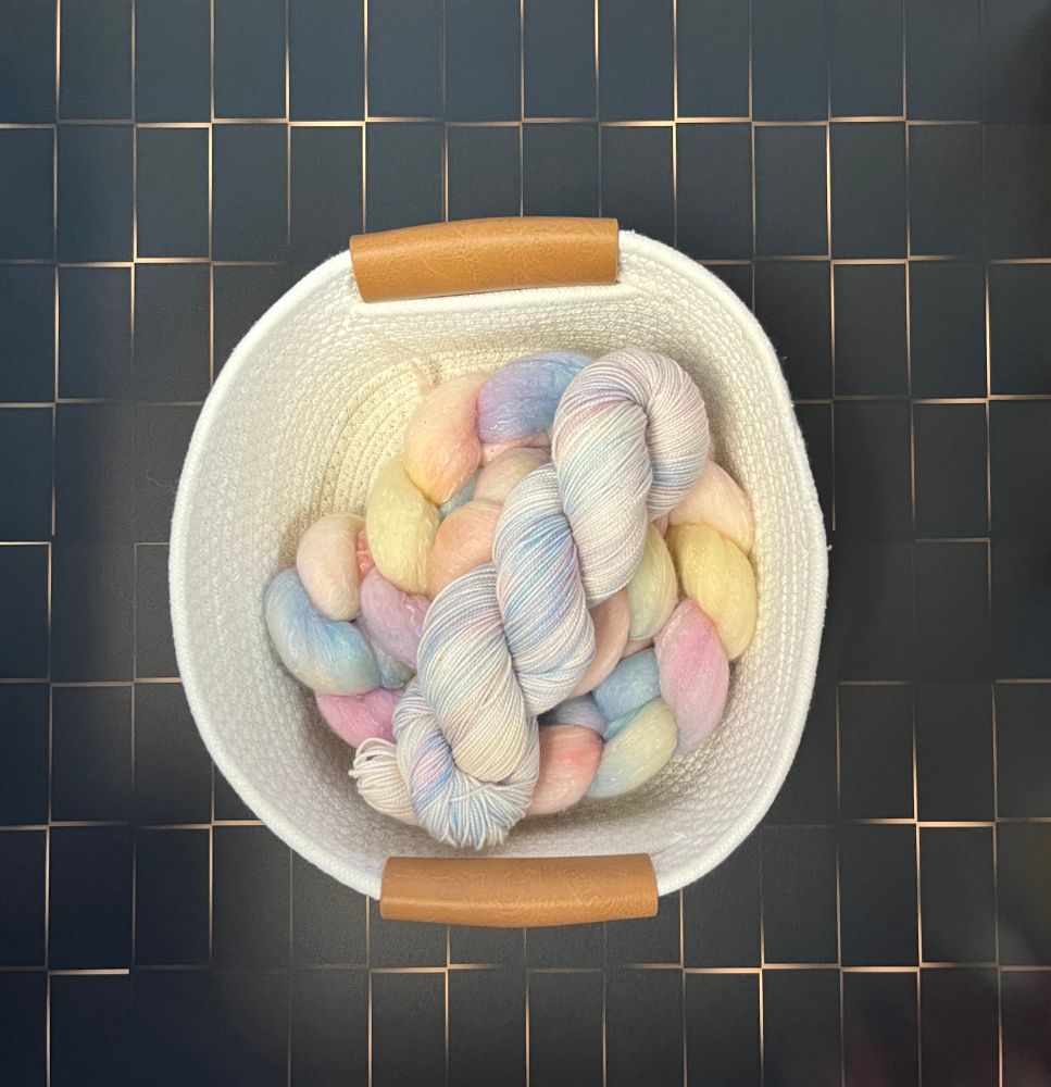Yarn and fiber in a basket. Both pastel variegated rainbow