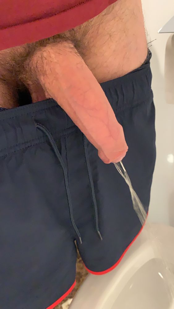 A semi hard penis pulled out of dark blue swimming shorts pissing forcefully.