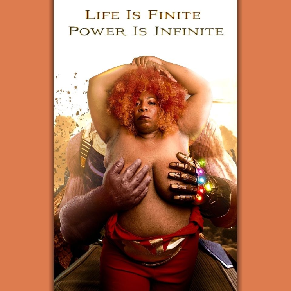 Image of TaLynn Kel, a topless fat Black woman with a red and orange afro standing between the legs of a large purple man. The right breast is cupped in a large purple hand while the left breast is held in a large hand wearing the infinity gauntlet. She is looking seductively at the camera. Her red jumpsuit with a gold phoenix on the front is pooled at her waist.