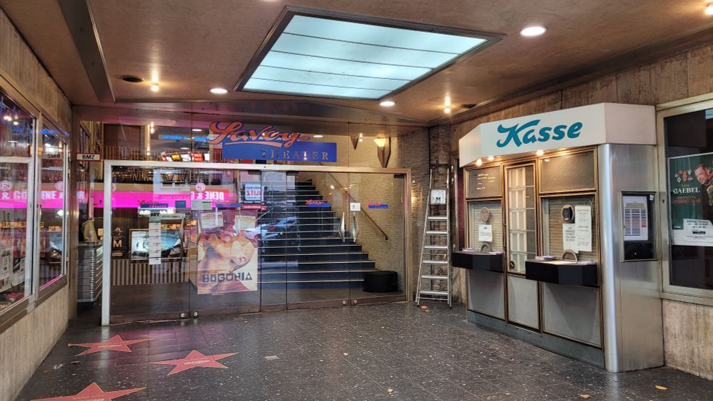 Überdachter Eingangsbereich des Atelier Kino im Savoy Düsseldorf. Viergliedrige Glastür, davor rechts ein altes Kassenhäuschen mit geschlossenen Rolladen.