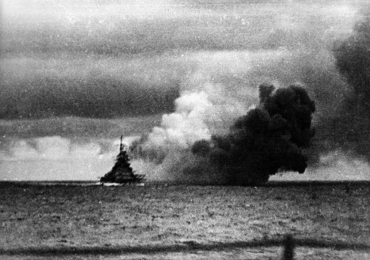 The Sinking of the Bismarck — A Final Blow in the Atlantic

This grainy black-and-white photograph captures the dramatic and chaotic moment of the German battleship Bismarck under heavy attack by British naval forces on May 27, 1941. Taken from a nearby pursuing vessel, the image freezes time as a towering column of dark smoke billows from near the ship’s stern, rising ominously against the overcast sky. The silhouette of the Bismarck can still be seen upright on the horizon, moments before her final demise. This was the climax of one of World War II’s most gripping naval chases. After sinking HMS Hood days earlier, Bismarck became the most wanted target in the Atlantic. Dozens of British warships, submarines, and reconnaissance aircraft were deployed in a relentless pursuit that spanned over 1,700 nautical miles. Crippled by a torpedo strike that jammed her rudder, Bismarck was unable to maneuver and soon faced the concentrated firepower of British battleships HMS King George V and Rodney. For over 90 minutes, she was pounded with hundreds of shells, many striking below the waterline. Yet despite the barrage, the Bismarck refused to sink. German sailors ultimately scuttled the ship to prevent her capture. Over 2,000 crewmen perished; only 114 survived. This image, stark and haunting, serves as a powerful visual of the brutal end of Germany’s most feared battleship. It also symbolized the fading dominance of the battleship era, which would soon be eclipsed by air power and submarines. For Britain, the destruction of the Bismarck was more than a strategic win—it was a morale boost in the dark days of 1941. The smoke curling into the sky is not just evidence of a naval defeat, but a turning point in maritime history, marking the end of an empire’s bold gamble on sea supremacy.