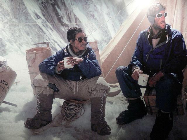 A Pause in the Death Zone – Humanity at the Edge of the World (1953)

In this colorized photograph taken during the 1953 British Mount Everest expedition, Tenzing Norgay and Sir Edmund Hillary sit outside a canvas tent nestled amid snow and ice, resting at one of the final high camps below the summit. The two men, clad in thick layers of wool and insulated jackets, cradle metal mugs—likely filled with warm tea or soup—symbolizing a rare moment of calm and human warmth in the perilous “death zone,” where oxygen levels are dangerously low and every movement drains energy. Ropes, oxygen canisters, and gear lie scattered around their boots, the organized chaos of a life lived on the edge. The diffused sunlight filtering into the frame, reflecting off snowy cliffs, imbues the image with a quiet dignity—a contrast to the monumental effort unfolding just beyond the camera’s reach.

This camp was one of several carefully staged support points designed by expedition leader John Hunt and his team. The use of supplemental oxygen, developed and refined by British engineers, played a critical role in enabling Hillary and Norgay to survive and thrive at such extreme altitudes. Their ability to pause, hydrate, and recover in such a hostile setting speaks not only to their individual strength but also to the detailed planning and teamwork that underpinned the expedition’s success. Moreover, the image hints at the often under-acknowledged labor of Sherpas like Norgay, whose intimate knowledge of the mountain and quiet endurance made the feat possible. In this photograph, we see not two legendary climbers poised for glory, but two men stripped to their essentials—sharing silence, struggle, and strength in a frozen world where life clings by threads.
