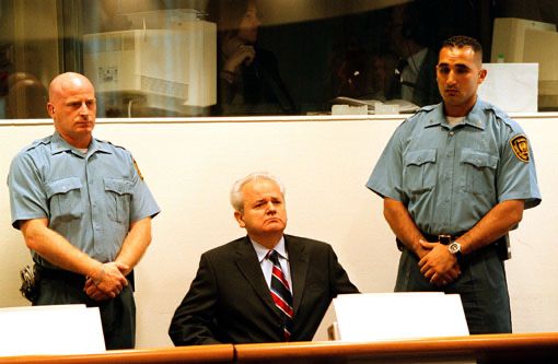Slobodan Milošević at The Hague – A President on Trial

This striking courtroom image captures Slobodan Milošević seated at the International Criminal Tribunal for the former Yugoslavia (ICTY) in The Hague, flanked by two stern-faced UN guards. Dressed in a black suit and red-striped tie, Milošević sits upright, exuding an air of defiance. This moment represents a profound shift in the post-Cold War international order. Taken during the early stages of his trial beginning in 2002, the image reflects the unprecedented legal accountability of a former head of state for war crimes, crimes against humanity, and genocide. The May 27, 1999 indictment against Milošević, issued while he was still in power, marked the first time such charges were brought against a sitting leader. It signaled a new era in global justice, wherein no office could shield one from prosecution for atrocities. This trial was a culmination of years of conflict across the Balkans—including Bosnia, Croatia, and Kosovo—where Milošević’s policies fueled ethnic cleansing, mass deportations, and systemic violence. In the courtroom, Milošević chose to represent himself, using the global stage to project his nationalist rhetoric while attempting to delegitimize the court’s authority. Behind the symbolism of the scene is a deeper evolution: the role of digital evidence, satellite imagery, forensic data, and cross-border witness testimony transformed the landscape of accountability. The trial was streamed globally, demonstrating how international institutions were evolving into more transparent and technologically integrated systems. Though Milošević died in 2006 before a verdict was reached, his prosecution remains a milestone in enforcing international humanitarian law. The image is not just about one man—it’s a visual testament to the world’s growing commitment to holding leaders accountable, regardless of their power or influence.
