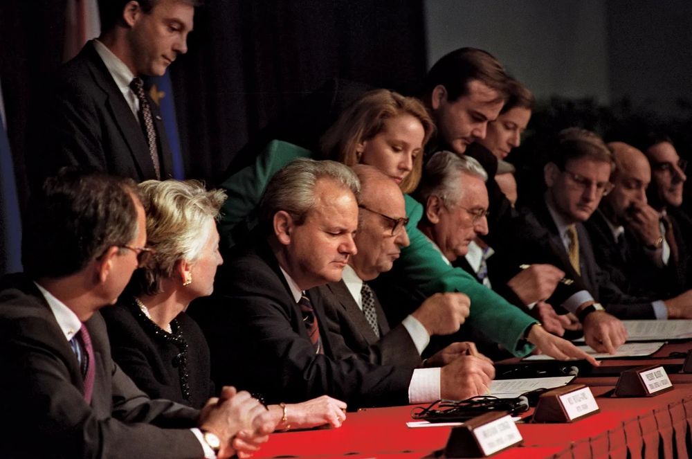 The Dayton Accords in Action – A Closer Look at Balkan Leaders & International Diplomats

This image captures a pivotal moment during the signing of the Dayton Peace Accords, a diplomatic agreement that officially ended the Bosnian War. At the center sits Slobodan Milošević of Serbia, deeply focused as he signs the document that would shape the future of the Balkans. Beside him are key leaders: Croatian President Franjo Tuđman and Bosnian President Alija Izetbegović, each representing opposing sides in one of the most devastating conflicts in post–Cold War Europe. Surrounding the main signatories are a host of aides and international negotiators, notably U.S. diplomat Richard Holbrooke and members of the European Union, guiding and observing the process with intense concentration. This captures not just signatures, but the delicate choreography of peace-making: every pen stroke and whispered consultation speaks to years of bloodshed, political maneuvering, and international intervention. Held in Dayton, Ohio, and finalized here in Paris in December 1995, the agreement ended a conflict that killed more than 100,000 people and displaced over two million. This image reflects the immense global effort to bring the war to a close, including the involvement of the United States, NATO, the EU, and the United Nations. Yet, the moment is also steeped in ambiguity—though it halted the violence, the Dayton Accords institutionalized ethnic divisions within Bosnia and Herzegovina’s governance structure. The contrast between weary Balkan leaders and composed Western diplomats is stark, symbolizing the imbalance of power and the external pressures that shaped the treaty. Milošević, in particular, appears pensive—his role in the war, once obscured by diplomacy, would soon be exposed on a world stage as the ICTY indicted him for crimes against humanity. This marked the beginning of a complex peace, built atop compromise, loss, and fragile hope for a multiethnic future in the Balkans