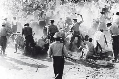 Brutal Repression – Police Crackdown During the Soweto Uprising

This harrowing black-and-white image captures the violent clash between apartheid police forces and Black South African protesters during the height of the Soweto Uprising in June 1976. In the foreground, uniformed officers wielding batons and rifles strike at a fleeing crowd, enveloped in a chaotic cloud of dust and panic. The officers, some mid-swing, wear helmets and boots, moving aggressively through a sea of civilians—many of whom appear to be students and bystanders caught in the melee. Their raised weapons and hostile posture contrast with the defenselessness of the people they attack, some of whom are on the ground, while others attempt to shield one another or retreat. In the background, the crowd stretches deep into the frame, underscoring the massive scale of the demonstration and the indiscriminate nature of the crackdown. This scene is emblematic of the state’s response to the uprising, which began on June 16, 1976, as a peaceful protest by schoolchildren against the enforced use of Afrikaans in Black schools. The government’s brutal suppression—resulting in the deaths of hundreds of students and the injury of thousands—marked one of the most traumatic turning points in South African history. This image lays bare the grim reality of apartheid-era policing, where armed force was used not just to maintain order, but to uphold a system of racial domination. The photograph stands as a visual indictment of institutional violence, reminding us of the cost of justice and the resilience of those who fight for it. In this image, the dust does not merely obscure—it becomes a symbol of erasure, resistance, and the long shadow of state-sanctioned brutality.