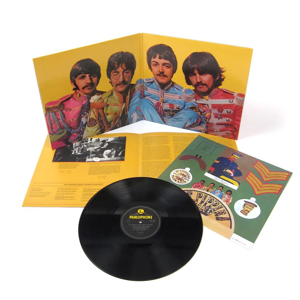 A Revolution in Packaging – Sgt. Pepper’s Gatefold and Vinyl Experience

This image showcases the Sgt. Pepper’s Lonely Hearts Club Band album in its iconic physical form: the gatefold vinyl package laid open, the black Parlophone LP prominently displayed, and colorful inserts spilling out. Released on June 1, 1967, this presentation marked a radical departure from conventional album packaging and redefined what a record could be. Inside the gatefold, a vivid portrait of the band members appears in their psychedelic military uniforms, this time against a golden yellow background. The reverse side features track listings, lyrics—a first for a major pop album—and production notes, placing emphasis on the album as a cohesive artistic statement. Surrounding the record are cut-out sheets featuring faux military badges, mustaches, and a cardboard cutout of the band’s fictional conductor, allowing fans to engage with the album’s concept in a tactile, imaginative way. Designed by artist Peter Blake and Jann Haworth, the album’s visual storytelling matched the boundary-pushing sounds etched into the vinyl grooves. The attention to detail in the packaging was revolutionary at the time, elevating the album from a mere music product to an immersive multimedia experience. The Sgt. Pepper vinyl wasn’t just heard—it was read, handled, studied, and performed with. This particular image captures that spirit of total artistry: the convergence of design, sound, and identity in a single format. With this release, The Beatles set a new standard for how albums could be conceived—as holistic works of art that invite the listener into a complete world. That ethos influenced countless musicians, designers, and fans in the decades that followed. The physical album became a canvas, a collectible, and a storytelling device. This photo crystallizes that historical moment, where pop culture met high concept and packaging became part of the performance.