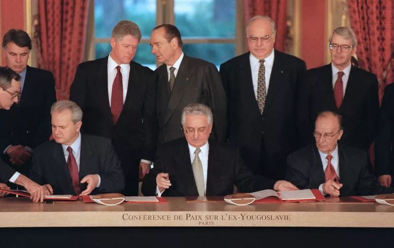 Signing the Dayton Accords – Fragile Peace in the Balkans

This historic image captures the formal signing of the Dayton Peace Accords in Paris on December 14, 1995, a pivotal event that brought an end to the brutal Bosnian War. Seated at the table are three central figures: Slobodan Milošević of Serbia, Franjo Tuđman of Croatia, and Alija Izetbegović of Bosnia and Herzegovina. Their expressions range from solemn to guarded, reflecting the weight of the moment and the deep wounds left by years of ethnic conflict. Behind them stand a host of international dignitaries, including U.S. President Bill Clinton, French President Jacques Chirac, German Chancellor Helmut Kohl, and British Prime Minister John Major—underscoring the global stakes and diplomatic pressure that forged this fragile peace. The gold-lettered backdrop reads “Conférence de Paix sur L’Ex-Yougoslavie” (Peace Conference on Former Yugoslavia), reinforcing the gravity of the occasion. This agreement, brokered at Wright-Patterson Air Force Base in Dayton, Ohio, and later formalized here in Paris, ended nearly four years of warfare in Bosnia that claimed over 100,000 lives and displaced more than 2 million people. The accords created a new constitution for Bosnia and Herzegovina, dividing it into two entities: the Federation of Bosnia and Herzegovina and Republika Srpska. The image represents not only a diplomatic breakthrough but also the complexities of peacemaking in the aftermath of genocide and ethnic cleansing. Milošević’s presence at the table would soon become symbolic—just four years later, he would be indicted for war crimes by the ICTY. This moment stands at the crossroads of diplomacy and justice, where peace was prioritized over punishment, at least temporarily. It marks the beginning of a post-war reconstruction era and serves as a visual reminder of both the power and limits of international negotiation in ending deeply entrenched conflicts.
