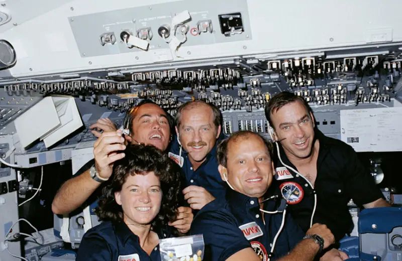 STS-7 Crew in Orbit – Teamwork Aboard Challenger

This image offers an intimate look inside the Space Shuttle Challenger during its historic STS-7 mission in June 1983. At the center foreground is Sally Ride, the first American woman in space, surrounded by her fellow crew members—Robert Crippen, Frederick Hauck, John Fabian, and Norman Thagard. The five astronauts, dressed in their navy NASA flight suits, are seen floating in zero gravity, smiling for the camera amid a backdrop of intricate switches, displays, and flight panels inside the shuttle’s flight deck. The camaraderie captured in their expressions reflects the spirit of collaboration and trust that defines successful space missions.

Launched on June 18, 1983, STS-7 was a landmark mission in many ways. It marked not only a critical advancement in U.S. crewed spaceflight but also demonstrated how diverse teams could thrive in high-stakes scientific environments. Ride operated the shuttle’s Canadarm to deploy and later retrieve satellites, solidifying the role of robotic technology in shuttle operations. The STS-7 mission also carried experiments designed to study the effect of space travel on various materials and biological samples, pushing forward both commercial and academic research.

The setting is rich with detail—overhead panels, communication headsets, floating pill containers—all representing the controlled chaos of life in orbit. Though visually informal, this captures a powerful message: the future of exploration depends on teamwork, adaptability, and breaking barriers. For many, it became the visual embodiment of NASA’s gradual shift toward inclusivity, not only welcoming women but preparing for a more collaborative and scientifically driven space program.

The mission ended safely on June 24, but its influence is ongoing. This photo, often featured in documentaries and educational materials, is more than just a snapshot of a crew—it’s a time capsule of a transformative era in human spaceflight.