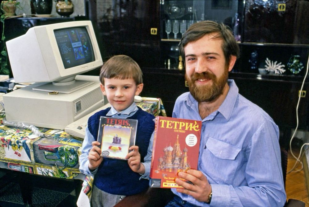 The Birth of Tetris – A Cold War Gaming Breakthrough

This vibrant image captures a moment of playful pride and historic innovation, as Soviet software engineer Alexey Pajitnov poses beside a young boy—likely a family member or young enthusiast—both holding early boxed versions of Tetris, the groundbreaking puzzle game Pajitnov created on June 6, 1984. Behind them, an old Soviet computer displays the game in action. What makes this photo so remarkable is its understated yet powerful reflection of a game that quietly transcended borders in a deeply divided world. Tetris was developed within the walls of the Soviet Academy of Sciences in Moscow at a time when Western and Eastern blocs were politically and ideologically at odds. Inspired by a traditional puzzle game called Pentominoes, Pajitnov simplified the gameplay into falling geometric shapes—tetrominoes—that needed to be rotated and fitted into complete lines. The game’s elegant logic, universal accessibility, and hypnotic pacing helped it leap beyond the Iron Curtain. Despite being state property in its early years due to Soviet copyright rules, Tetris found its way to Hungary, and soon to the West, becoming a hit across PCs, arcade cabinets, and most famously, Nintendo’s Game Boy in 1989. It was the first game exported from the USSR to the U.S., and its mass appeal demonstrated the unifying potential of digital entertainment in an era of political estrangement. In the photo, the juxtaposition of childlike innocence, retro computing, and Soviet innovation visually embodies the cultural permeability of great ideas. Decades later, Tetris remains one of the most beloved and best-selling video games of all time, a rare Cold War relic that brought joy rather than tension to millions.
