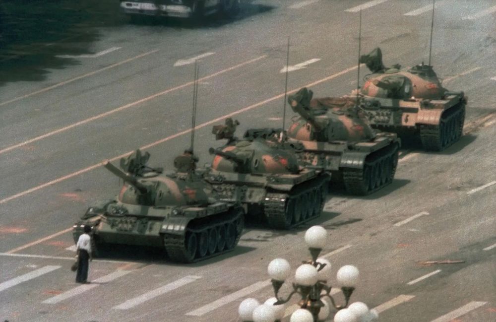 “Tank Man” and the Tiananmen Square Protests of 1989

This historic image captures an anonymous man standing defiantly in front of a line of Chinese Type 59 tanks on June 5, 1989, during the aftermath of the Tiananmen Square protests in Beijing. Known globally as “Tank Man,” the lone figure became an enduring symbol of individual resistance against authoritarianism. The man, holding shopping bags in each hand, stepped into the path of the tanks shortly after the Chinese government launched a violent military crackdown to suppress weeks of pro-democracy protests. These protests, led by students and supported by intellectuals and workers, had occupied Tiananmen Square for nearly two months, demanding political reform, anti-corruption measures, and greater freedoms. The Chinese government declared martial law and, on June 3–4, deployed troops and armored vehicles into the city. Hundreds—possibly thousands—of unarmed civilians were killed in what became one of the most infamous suppressions of dissent in modern history. Despite the government’s efforts to erase the event from domestic memory, the image of “Tank Man,” taken by photographer Jeff Widener from a nearby hotel balcony, was smuggled out and widely published internationally. It has since become a universal emblem of courage and nonviolent protest. The man’s identity and fate remain unknown, adding to the mystique and poignancy of the moment. In the broader historical context, this image underscores the power of visual media in shaping global awareness of human rights violations and remains one of the most iconic photographs of the 20th century.