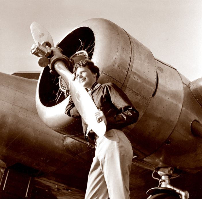 Amelia Earhart with Her Lockheed Electra – A Portrait of Pioneering Spirit

In this evocative sepia-toned photograph, Amelia Earhart is seen leaning affectionately against the propeller of her Lockheed Electra 10E, the aircraft she would later pilot during her final around-the-world attempt in 1937. The image captures not just a moment of calm before a great challenge but an enduring symbol of human ambition, technological progress, and personal resolve. Earhart, dressed in practical slacks and a buttoned-up blouse, gazes contentedly toward the horizon, her hand resting gently on the polished propeller blade. Her body language conveys deep familiarity with the machine behind her—an embodiment of the harmony she achieved between pilot and aircraft.

The Lockheed Electra, with its twin radial engines and advanced all-metal design, represented cutting-edge aviation technology of the 1930s. It was specially modified for Earhart’s ambitious circumnavigation of the globe, outfitted with extra fuel tanks and advanced navigation systems for long-distance flight. The aircraft’s engine cowling, propeller assembly, and meticulously riveted fuselage glisten in the sunlight, reflecting the industrial optimism of an age that looked skyward for its heroes. This photograph likely dates from 1936 or early 1937, during Earhart’s meticulous preparations for the historic journey that would ultimately end in mystery and international fascination.

Amelia’s serene expression and relaxed posture reveal her deep confidence and passion for flight, even in the face of looming uncertainty. As one of the most famous aviators of her era, Earhart’s relationship with her aircraft symbolized the possibilities that aviation offered for transcending gender roles, geographical limits, and societal expectations. Her pioneering efforts not only broke records but inspired millions—this image freezes one such moment of inspiration in time, reminding us of the boldness it takes to reach for the unknown.