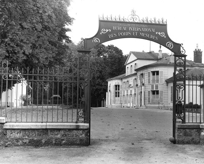Founding Site of Global Measurement – The Bureau International des Poids et Mesures

This black-and-white image captures the historic entrance of the Bureau International des Poids et Mesures (BIPM) in Sèvres, France, framed by a wrought-iron gate with ornate scrollwork and the institution’s name prominently displayed in French: “Pavillon de Breteuil – Bureau International des Poids et Mesures.” The building seen through the archway is the Pavillon de Breteuil, an 18th-century structure repurposed to house one of the most consequential scientific organizations in modern history. This site became the global headquarters for metrology after the signing of the Metre Convention on May 20, 1875, an international treaty that established a universal framework for standardizing measurements across nations. The agreement initially included 17 countries—now expanded to nearly 60—and formed the foundation of the metric system’s worldwide adoption.

The BIPM was tasked with maintaining prototype standards, including the international prototype of the metre and the kilogram. These physical standards were stored under strict environmental conditions within the building depicted, symbolizing the global commitment to scientific accuracy and consistency. Over time, these prototypes evolved into more precise definitions based on physical constants, but the BIPM remains the core steward of international measurement standards today. This image thus represents more than a gateway—it marks the institutional birthplace of the International System of Units (SI), influencing everything from scientific research and space exploration to trade, medicine, and daily life around the globe. The quiet elegance of the archway belies the immense impact the decisions made behind it have had on unifying how humanity measures and understands the world.