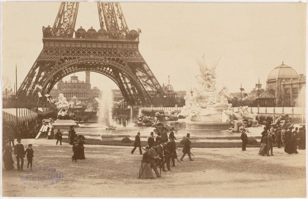 The Eiffel Tower at the 1889 World’s Fair – Paris Embraces Modernity

This sepia-toned photograph captures the Eiffel Tower during its debut at the 1889 Exposition Universelle, held in Paris to commemorate the 100th anniversary of the French Revolution. Rising proudly in the background, the tower forms a commanding archway over a grand plaza teeming with ornate fountains, classical sculptures, and bustling crowds. Visitors dressed in 19th-century fashion—top hats, bonnets, parasols—wander the fairgrounds beneath the tower’s iron legs, marveling at a structure unlike anything the world had seen. Designed by Gustave Eiffel, the tower was not originally built to last—it was expected to stand for only 20 years. Yet in this image, it already exudes permanence.

The photograph showcases the cultural transformation taking place in France at the end of the 19th century. Here, Paris stands at the crossroads of tradition and innovation: Greco-Roman statues and baroque fountains surround a structure made entirely of wrought iron, symbolizing a break from stone and classical norms. The 1889 fair was a showcase of industrial progress, and the Eiffel Tower stood as its centerpiece—an engineering feat that signaled France’s role at the forefront of technological advancement. Its lattice design, both daring and efficient, exemplified a new architectural language born from science, mathematics, and machine precision.

Though critics initially decried it as an “iron monstrosity,” the public’s awe was palpable. Over two million people visited the tower during the exposition, ascending via hydraulic elevators to view the Paris skyline from a new, modern height. What once shocked the senses came to define a generation’s aspirations. This photo captures the very moment when skepticism gave way to admiration—when art met engineering, and the Eiffel Tower became more than a temporary exhibition piece. It became a lasting icon of elegance forged from iron and vision.