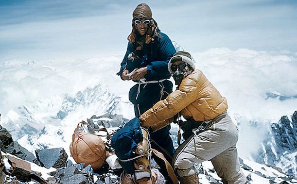 Above the Clouds – The Summit Moment of Everest’s First Ascent (1953)

This rare color photograph captures Sir Edmund Hillary and Tenzing Norgay near the summit of Mount Everest on May 29, 1953, during their groundbreaking ascent. Surrounded by a breathtaking panorama of snow-covered Himalayan peaks and a sea of clouds stretching endlessly below, the climbers are seen adjusting gear and taking brief respite after reaching the world’s highest point. Both are dressed in thick, insulated clothing—Hillary in a dark blue down suit and Norgay in a mustard yellow jacket—with oxygen masks and tanks secured, highlighting the crucial role technology played in their success. The scene is one of awe, exhaustion, and triumph, symbolizing the moment humankind first stood atop the 8,848-meter giant.

Though lacking in modern satellite communications and GPS, the 1953 British expedition relied on innovative equipment for the time. New designs in oxygen delivery systems made high-altitude survival viable; clothing composed of lightweight synthetic and natural fibers allowed better movement while retaining warmth. This photo immortalizes not just their physical ascent, but a technological and logistical victory that opened new frontiers in mountaineering. It also underscores the equal credit both men received in the wake of their feat, though later records clarified that Hillary was the first to step on the summit. Tenzing’s achievement—breaking barriers for indigenous Sherpas often relegated to supporting roles—elevated him to national hero status in Nepal and India. Their teamwork, captured at this thin-aired pinnacle of the world, remains an enduring example of what’s possible when resilience, trust, and innovation unite in the harshest environments Earth has to offer.