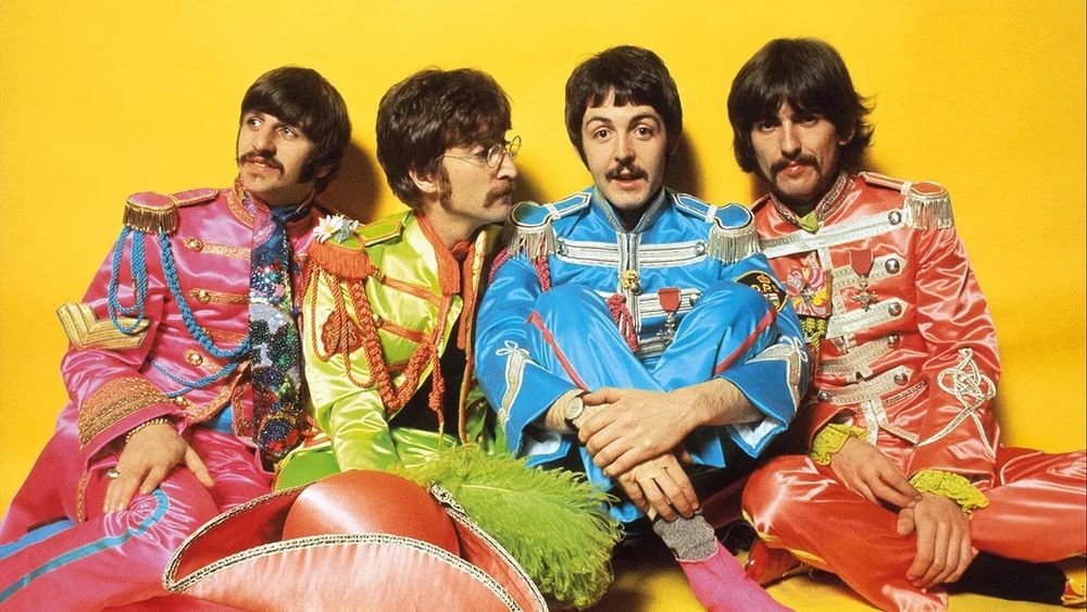 The Beatles in Full Technicolor – Icons of the Summer of Love

This vivid image shows The Beatles seated against a bright yellow background, dressed in the flamboyant satin military uniforms featured on the Sgt. Pepper’s Lonely Hearts Club Band album cover. From left to right: Ringo Starr in hot pink, John Lennon in lime green, Paul McCartney in sky blue, and George Harrison in crimson red. The photo was part of the official promotional campaign for the album, which released on June 1, 1967, and quickly became a cultural phenomenon. Their costumes—embellished with epaulets, tassels, and medals—were more than stage wear; they were a visual representation of the band’s departure from traditional pop and embrace of theatrical alter egos. The “Sgt. Pepper” concept allowed them to experiment musically and visually, unbound by their earlier image. This particular promotional photo became one of the defining images of the Summer of Love. It emphasized not only their new sound but also the psychedelic aesthetic and anti-establishment values of the era. Each member’s expression is relaxed yet distinct, reflecting their evolving artistic personalities. Paul’s front-facing posture with arms resting over his knees gives him a focal presence, underscoring his central role in conceptualizing the album. The bright color palette and exaggerated styling mirrored the visual experimentation of 1960s psychedelia and pushed the boundaries of what a rock band could represent. This photo helped transform The Beatles from pop celebrities into countercultural icons, reinforcing the album’s conceptual framework and its blend of surrealism, satire, and sonic adventure. Capturing the tension between playfulness and reinvention, this image became an enduring symbol of one of the most influential artistic reinventions in modern music history.
