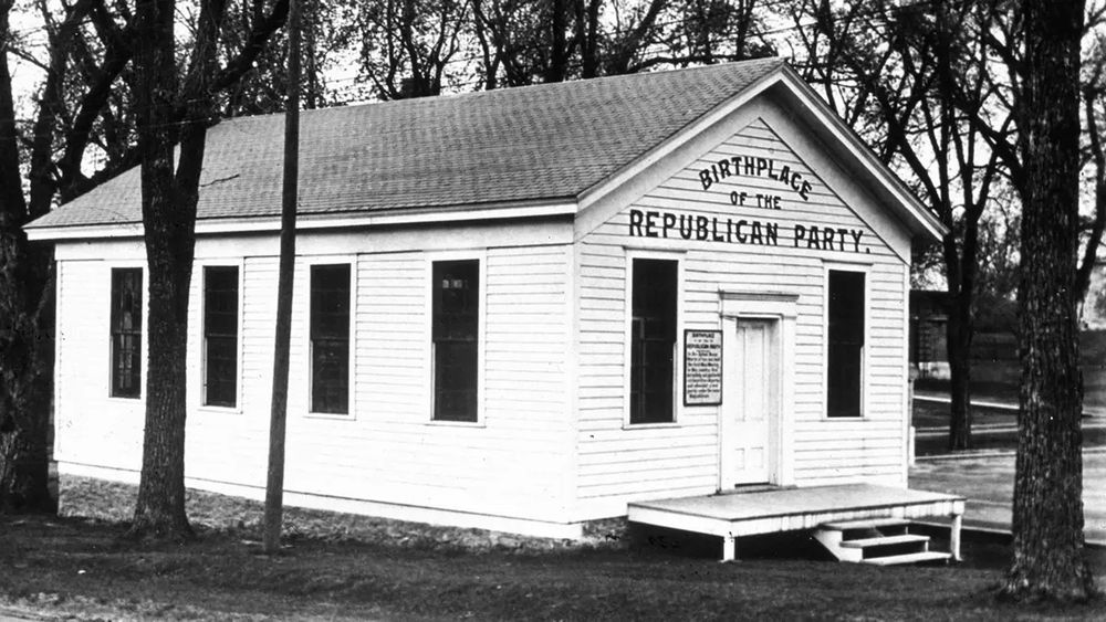 The Birthplace of the Republican Party

A black-and-white historical photograph of a small wooden schoolhouse in Ripon, Wisconsin, with the words “Birthplace of the Republican Party” painted in bold letters on the front facade. The modest structure, surrounded by bare trees, stands as a monument to a pivotal moment in American political history. On March 20, 1854, abolitionists, former Whigs, and Free Soilers gathered inside to oppose the expansion of slavery into new territories under the controversial Kansas-Nebraska Act. Their meeting gave rise to the Republican Party, a movement that would reshape the national political landscape. The schoolhouse symbolizes the party’s grassroots origins, born from moral convictions rather than political expediency. Within a few years, this newly formed party would challenge the dominance of pro-slavery Democrats, ultimately leading to the election of Abraham Lincoln in 1860. The stark simplicity of the building underscores the powerful influence of ordinary citizens uniting for a cause, demonstrating how political movements can begin in the most unassuming settings yet wield enormous influence over history. Today, the site remains preserved as a historical landmark, a testament to how a single meeting in a one-room schoolhouse transformed American politics and set the nation on a course toward the Civil War.