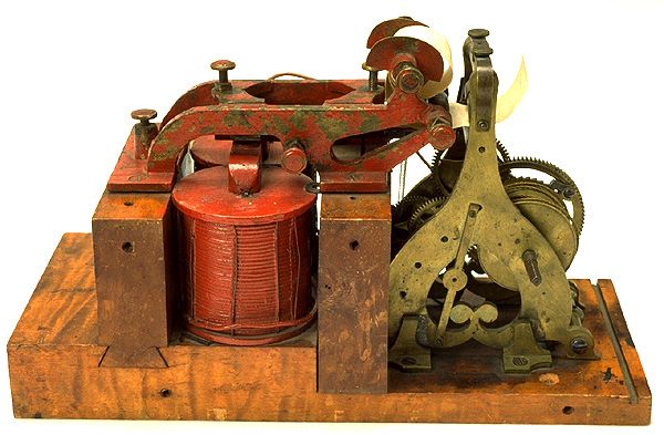 The Original Telegraph Device Used by Samuel Morse

This image showcases the original electromagnetic telegraph instrument developed by Samuel Morse and Alfred Vail, the very device used on May 24, 1844, to send the first long-distance message from Washington, D.C., to Baltimore. The design is remarkably compact yet ingenious, consisting of a red-painted electromagnet coil, wooden base, iron armature, and a mechanical gear-driven paper tape system that recorded the dots and dashes of Morse code. The simplicity of its components belies its revolutionary impact on communication and technology. Before this invention, the fastest way to transmit messages over long distances was by horse or ship, which often took days or weeks. The electromagnetic telegraph compressed space and time, enabling the near-instantaneous transfer of information across continents. The device in the image represents not just a tool but the physical beginning of the information age. Its construction reflects early 19th-century American engineering, resourceful and minimalist in form, yet profoundly effective. The telegraph’s mechanism converted electrical impulses into physical markings on a continuous paper strip—code that could be decoded by trained operators. This ability to digitize language into a sequence of short and long electrical signals laid the foundation for all subsequent forms of digital communication. Morse and Vail’s telegraph revolutionized journalism, finance, and military coordination, enabling messages to traverse borders and oceans faster than ever imagined. Its success led to the rapid spread of telegraph lines across the United States and Europe, forming the first global communications network by the late 19th century. This specific device is not only a marvel of innovation but a cultural artifact—testament to the moment when human voices first began to travel via electricity, signaling a new epoch in how societies share knowledge, coordinate actions, and record history.