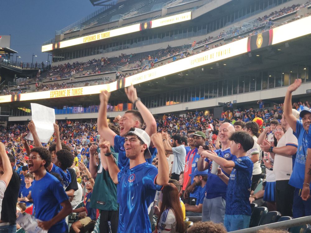 I group of Chelsea FC supporters in mostly blue shirts yelling and cheering after a Chelsea goal