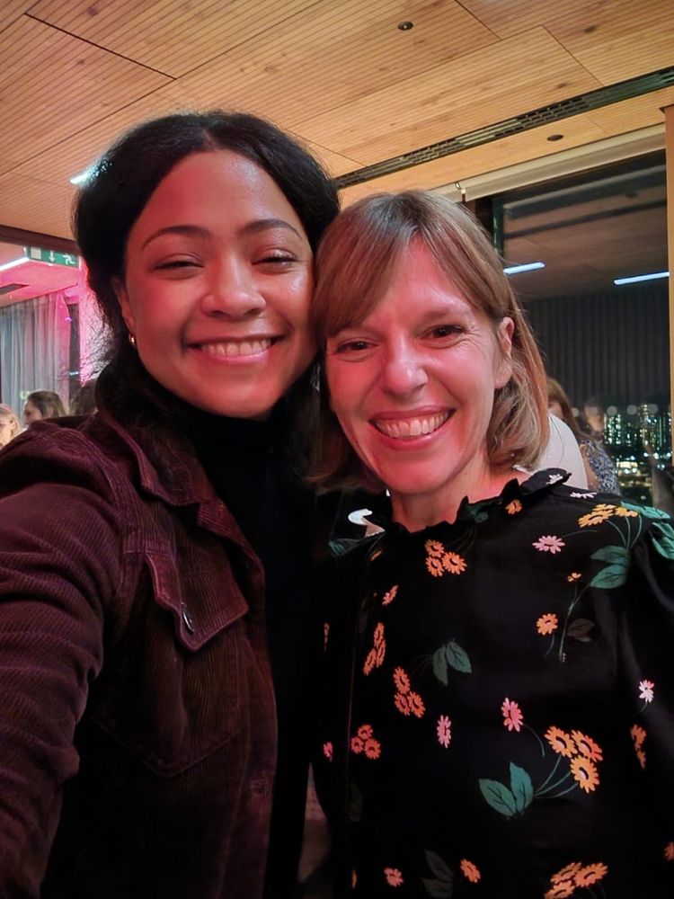mixed heritage woman in maroon jacket and white woman in floral dress smile at the camera
