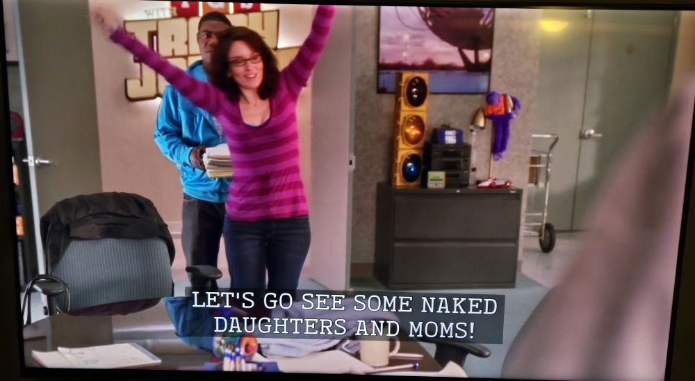 Liz Lemon, played by Tina Fey, saying "Let's go see some naked daughters and moms!" With her arms raised up in celebration 