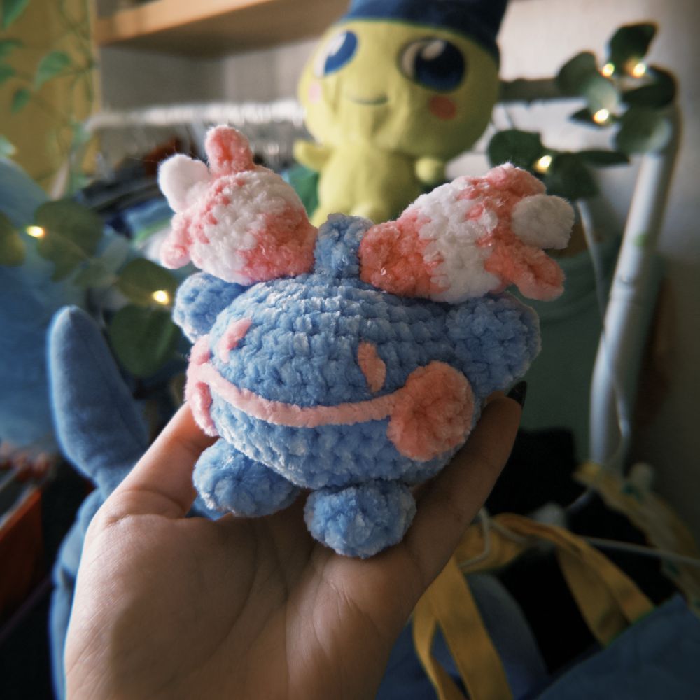 A super soft chenille crochet plushie of the pokemon chingling, in the trans colours! They have a bell inside and make little chime sounds 💖