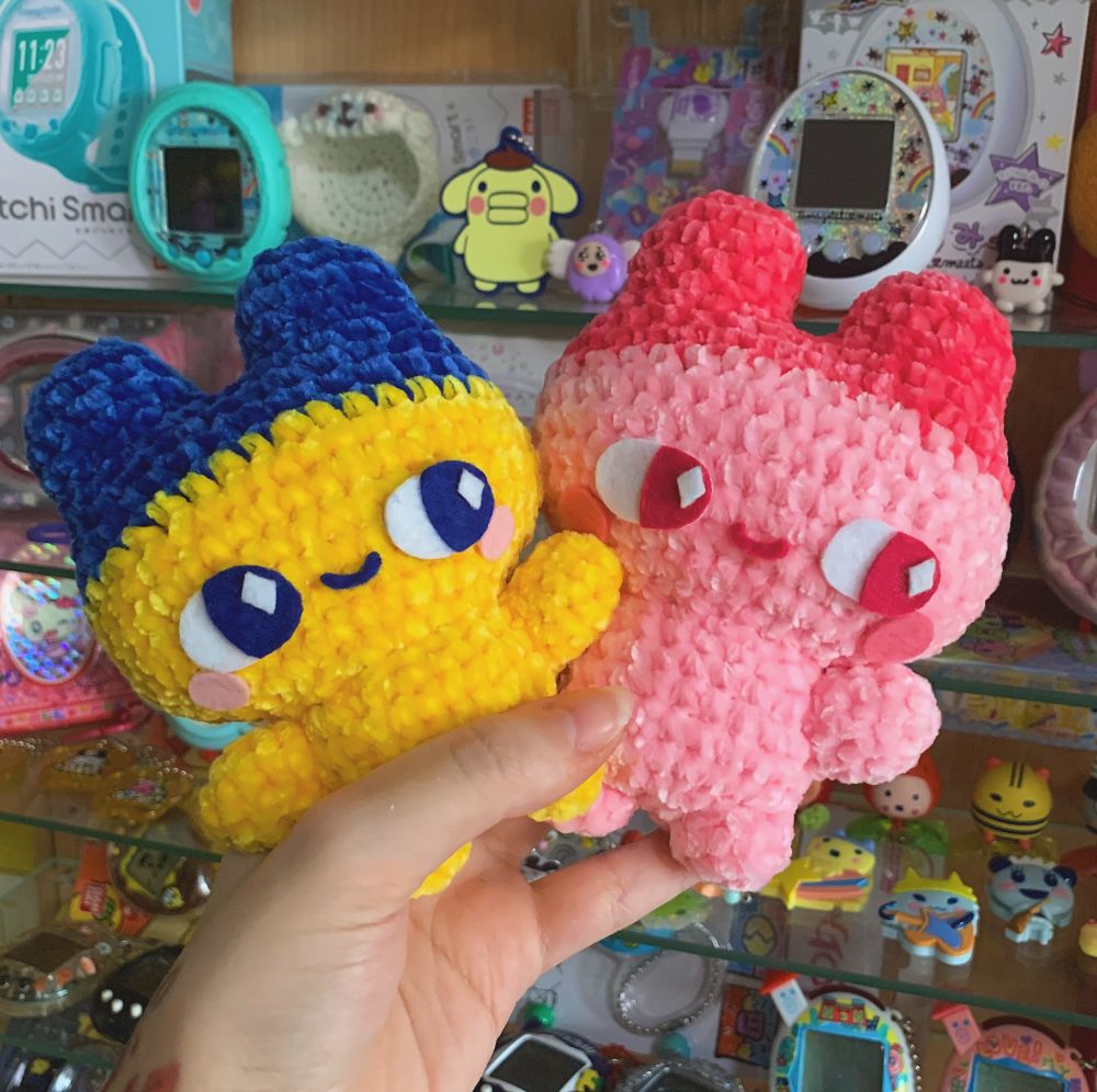 Two crochet amigurumi plushies, also made from soft and squishy chenille. They're both the tamagotchi character Mametchi, the left one is in the original colours and the right one is the sakura version