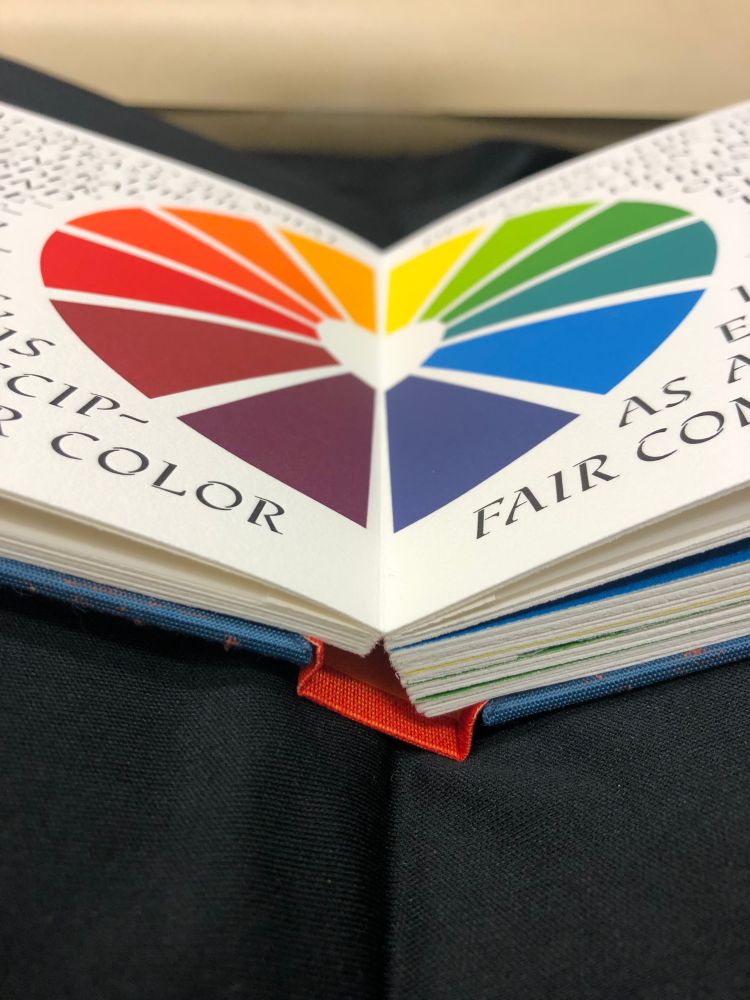 Image of an open book with a centered chromatic wheel. The image is angled so that the chromatic wheel appears as a rainbow heart.