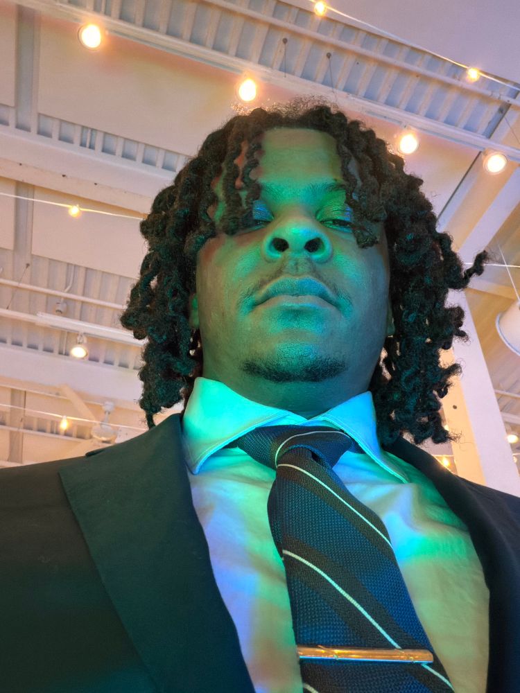 Man standing looking over camera. He is wearing a suit and tie. 