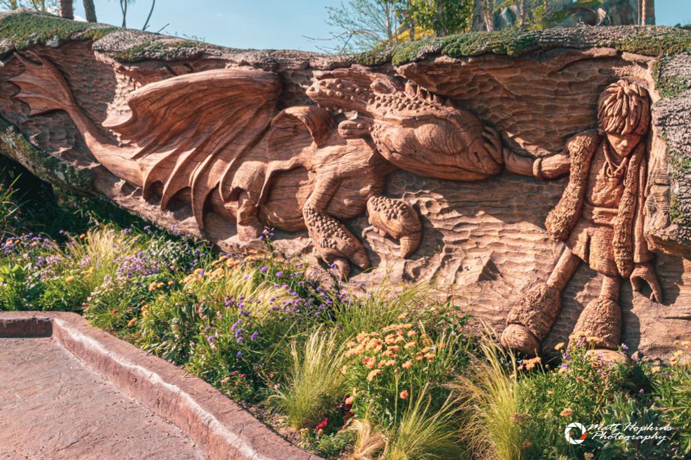 Wood carving of Hiccup meeting Toothless surrounded by wildflowers