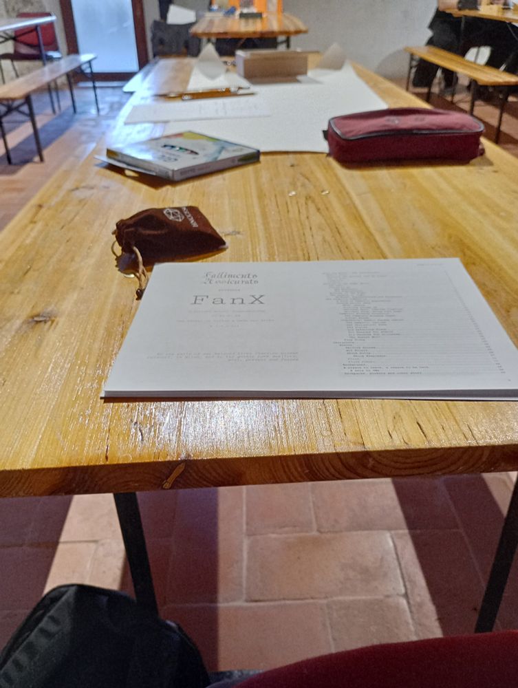 A wooden table, set with a huge strip of paper, dice, pencils and a home-printed manual titled "FanX"