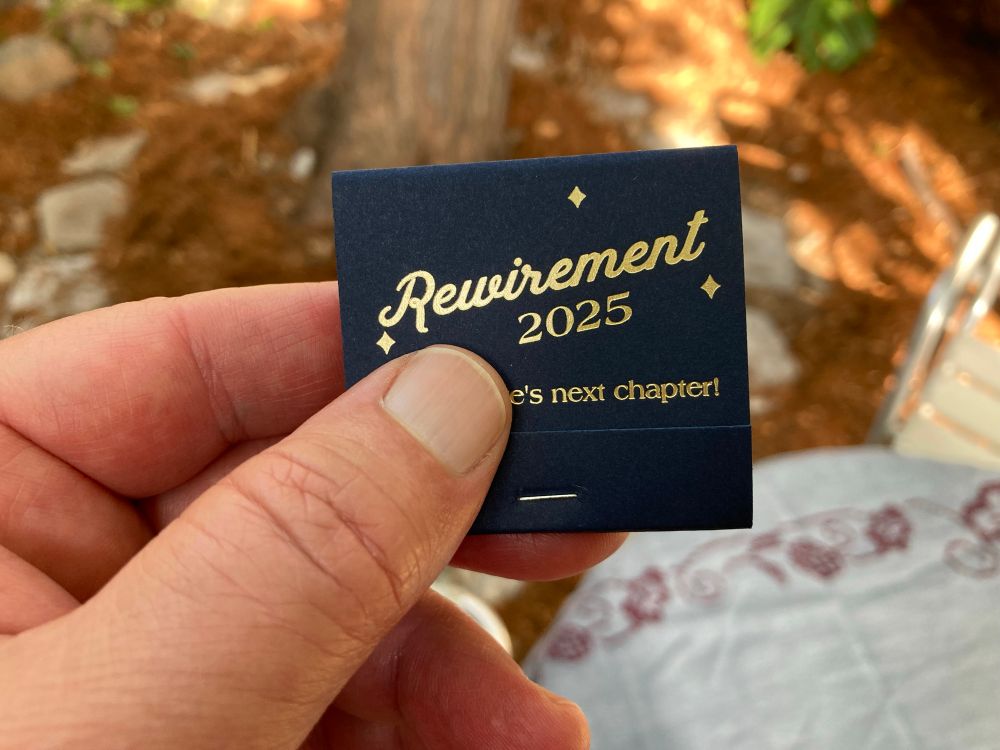 A blue matchbox with writing on the front. The visible part says “Rewirement 2025 — [redacted]’s next chapter”