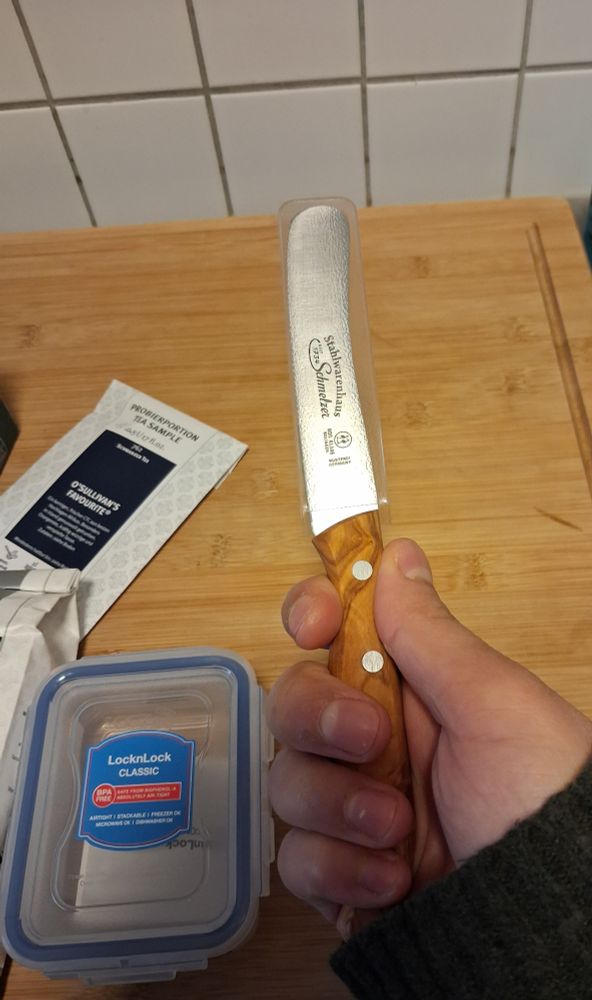 Meine Hand hält ein Messer mit Holzgriff. Links sieht man eine kleine Plastiktupperbox