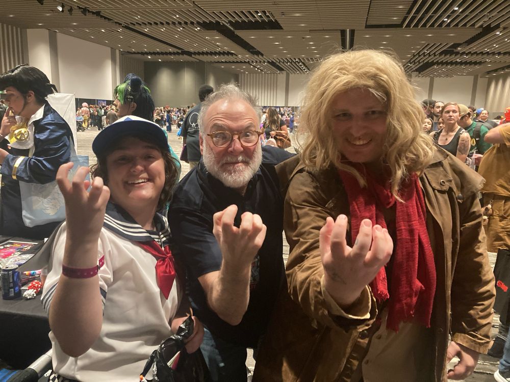 Two cosplayers pose with voice actor Richard Horvitz between them. All three have their hands up making an Invader-Zim-esque pose.