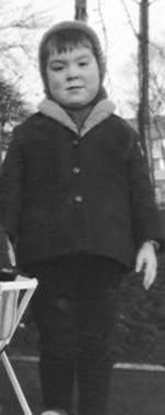 Me in c1965 in a balaclava and winter coat standing by my younger brother's pushchair in a park