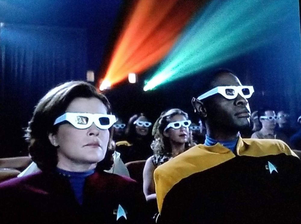 Janeway, Tuvok and the rest of the Voyager crew in a theater wearing rudimentary cardboard 3D glasses