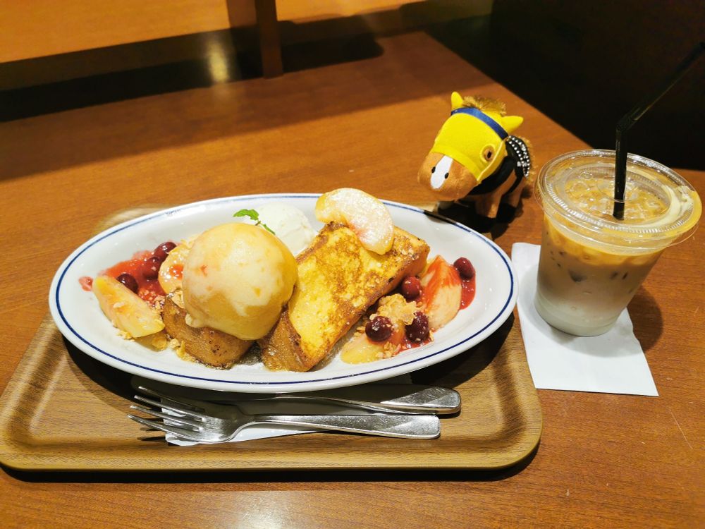 白桃がのったフレンチトーストを見つめるボルドグフーシュのマスコット。近くにはアイスカフェラテの入ったカップが置かれている。