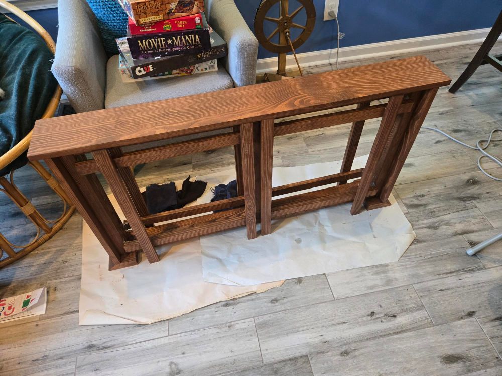 dark wooden table about 6 inches wide and 25" tall.  folded under the table are two legs with two vertical supports and two horizontal supports. the legs are folded under the table.