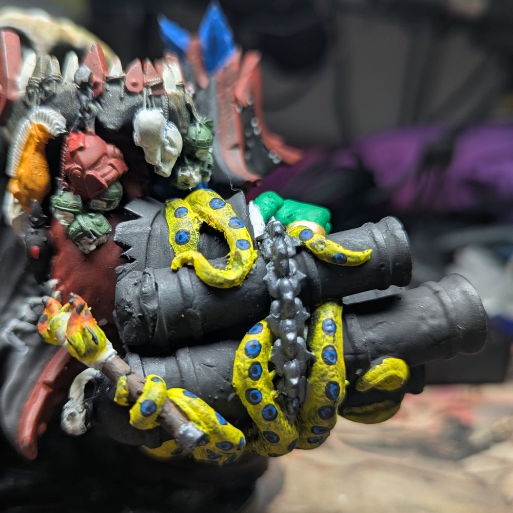 Closeup of the side of the cannon arm, showing tentacles wrapped around it. One of them holds a lit torch near the fuses of the cannons.