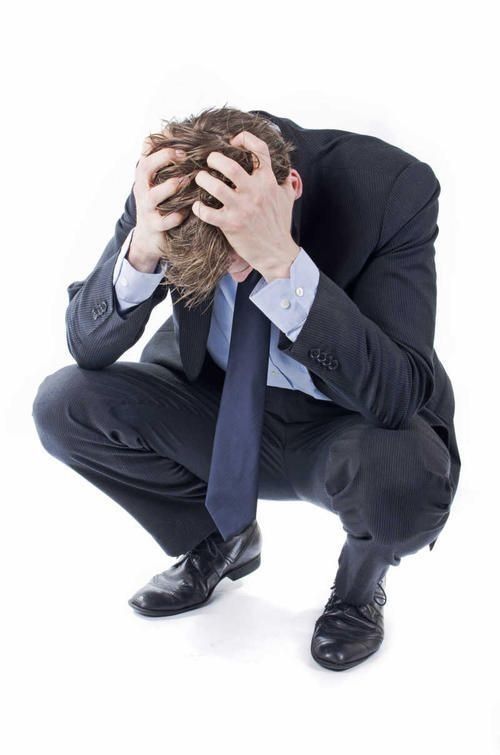 Imagen de stock de un señor acuclillado sujetándose la cabeza con una crisis existencial tremenda 