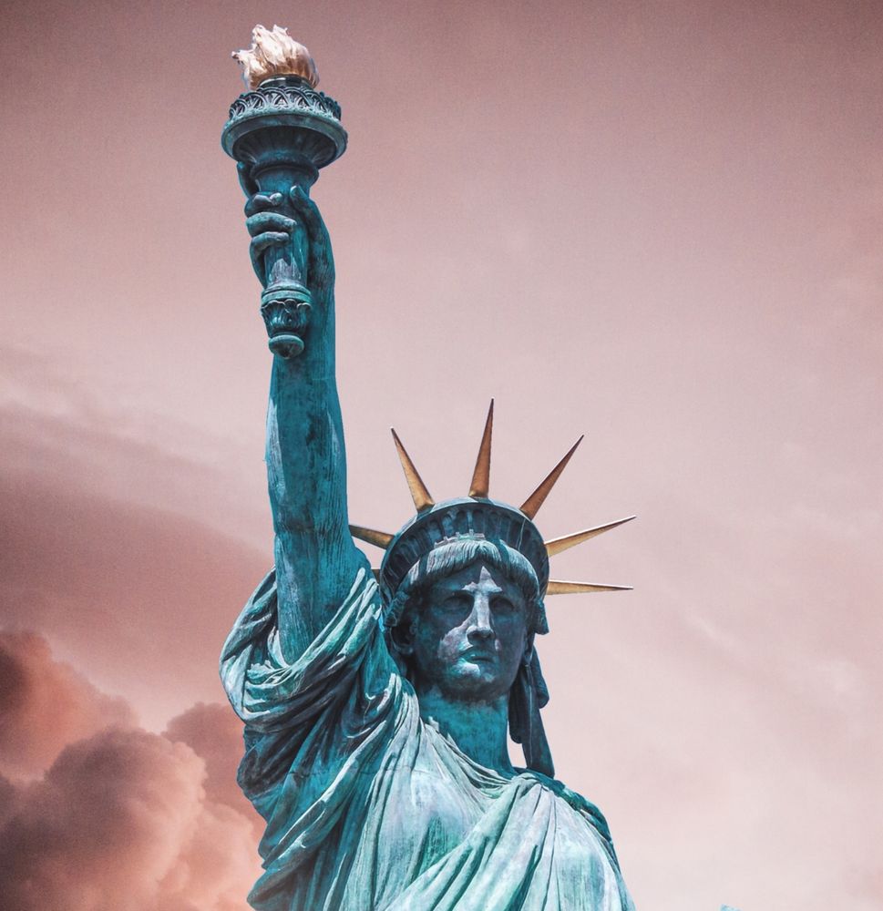 Gesicht und Arm der Lady Liberty vor einem leicht hellroten Hintergrund. 