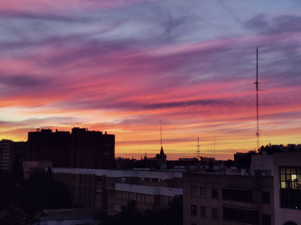 Skyline desde la ventana de la oficina a contraluz con el cielo bañado por infinidad de tonos azules, amarillos, rojos y rosas del amanecer y las nubes difuminadas