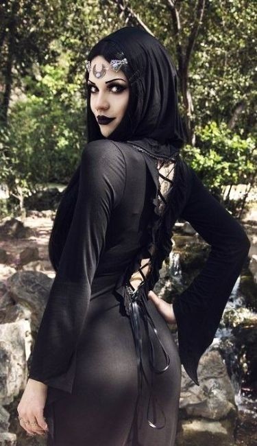 Colour photo of Mary de Lis in a woodland setting. She is wearing a black dress fastened at the back with black ribbon, and is looking over her shoulder.