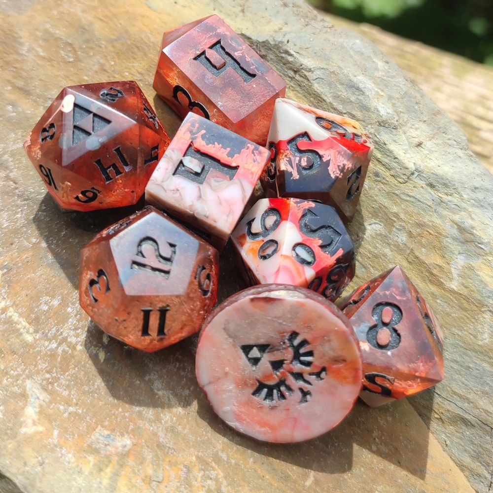 A red/orange firey coloured 7 piece set of handmade polyhedral dice with a coin. The coin and d20 face show the triforce from the legend of zelda. They are inspired by Death Mountain.